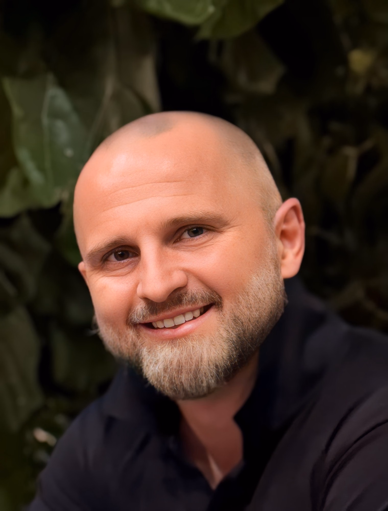 Michael Blackhurst, smiling, in a dark shirt against green leaves